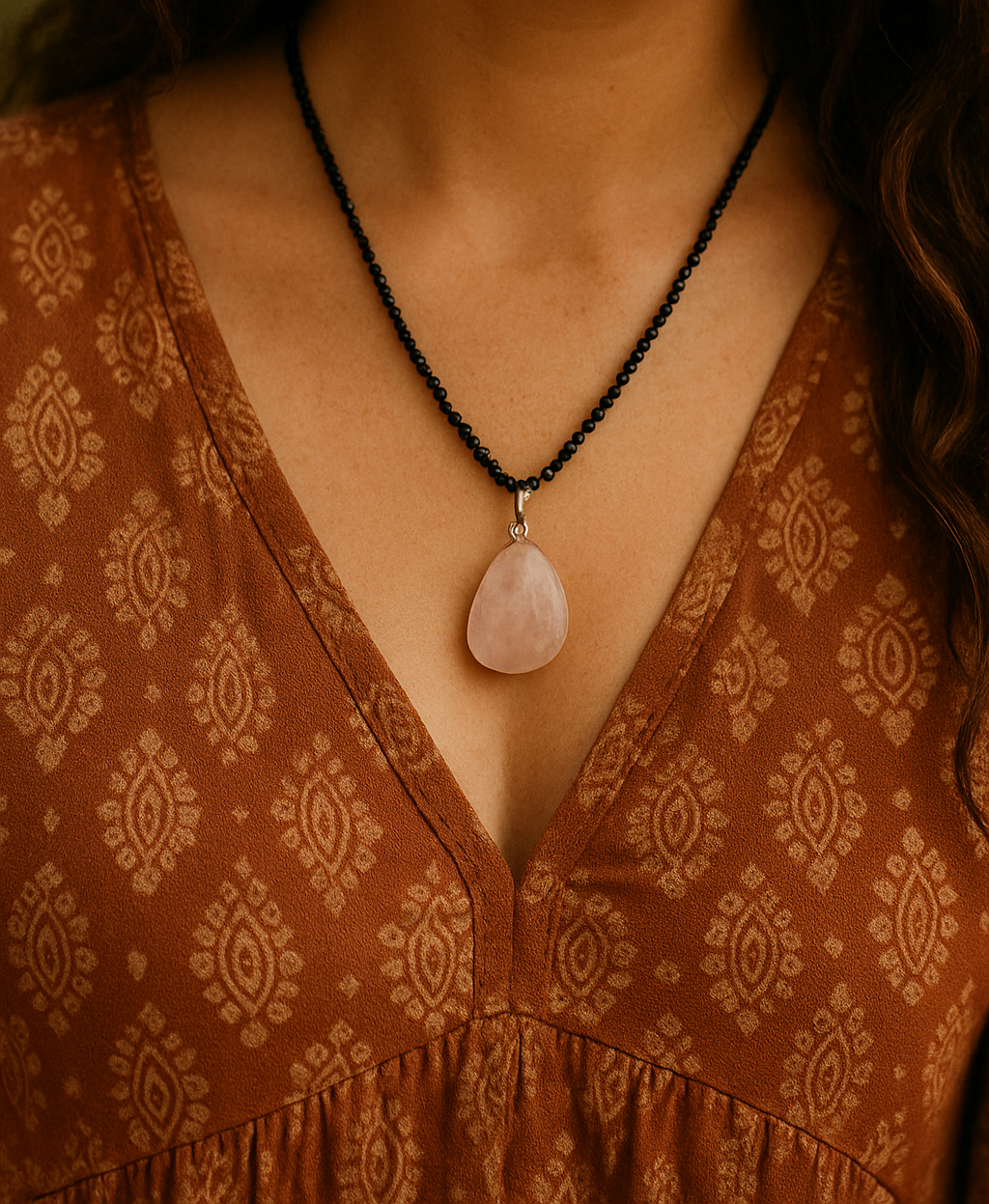 Person wearing a patterned dress with a necklace featuring a pink stone pendant.